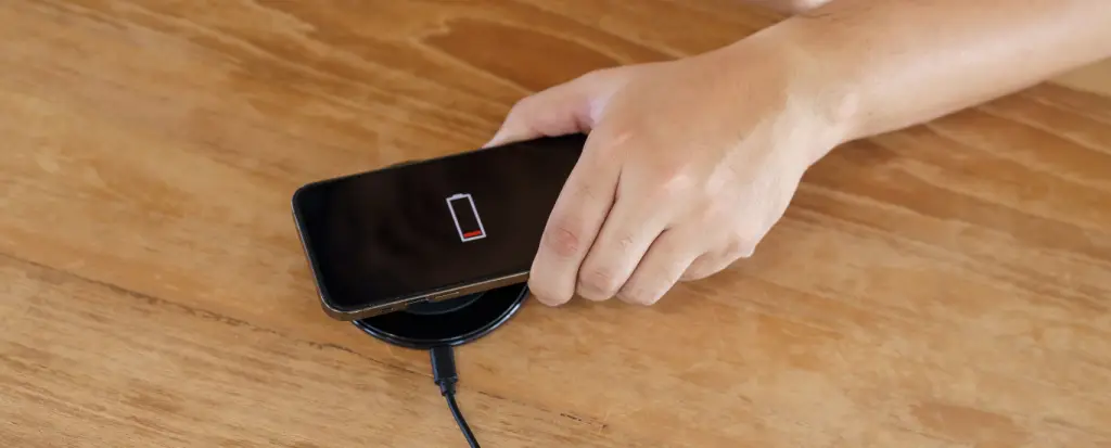 Hand placing a smartphone with a low battery warning onto a wireless charger on a wooden table.