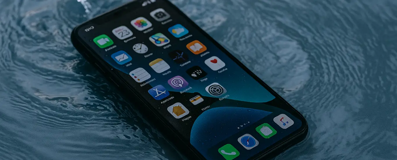 Smartphone lying in water with the screen still on, showing app icons.